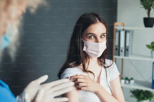 病院でマスクを着けてコロナウイルスワクチンを接種しながらカメラを見ている愛らしい女性