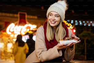 Porträt einer glücklichen Frau, die Donuts isst und den Weihnachtsmarkt genießt. Feiertagsweihnachten Menschen Spaßkonzept