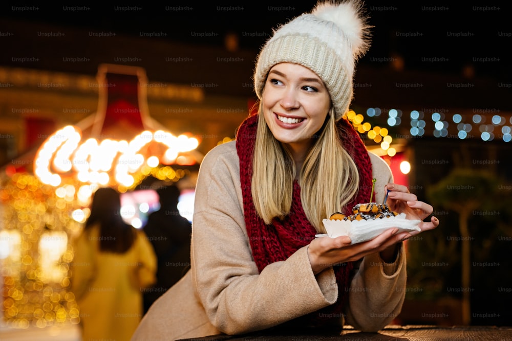 Portrait of happy woman girl eating donuts and enjoying christmas market. Holiday christmas people fun concept