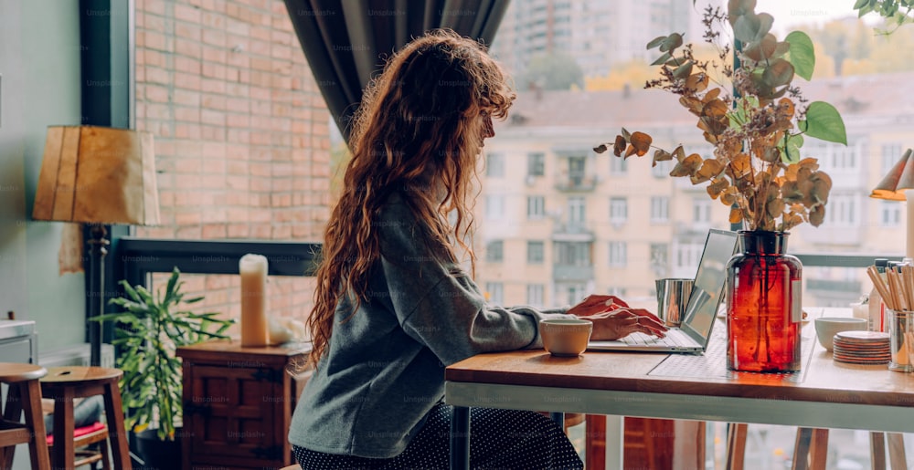 Mulher nova com cabelo encaracolado trabalhando no escritório remoto do café usando laptop. Banner panorâmico. Foco seletivo.