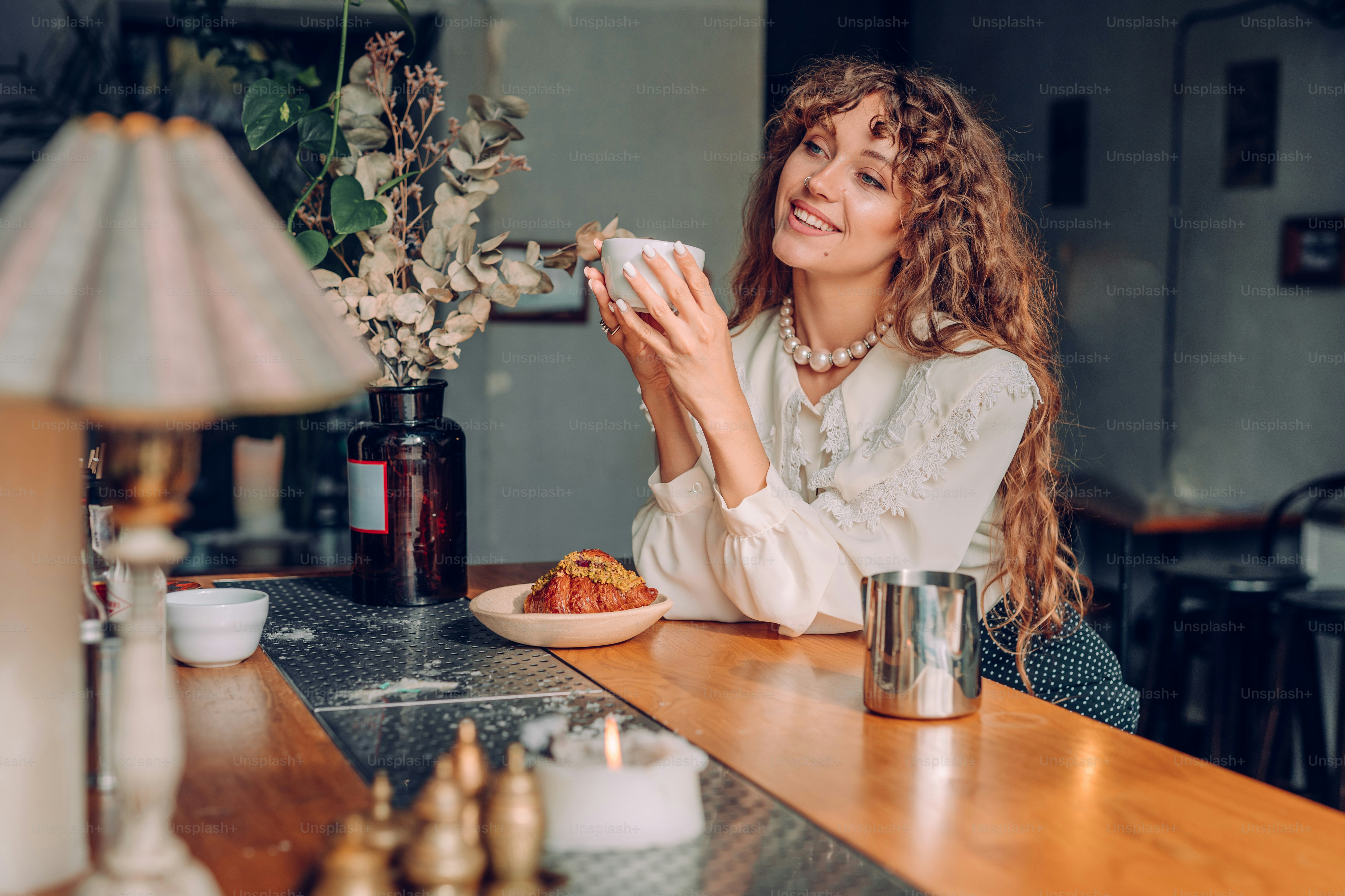 Lächelnde junge Frau mit lockigem Haar im Vintage-Stil genießen Tee im Café. Selektiver Fokus auf die Frau.