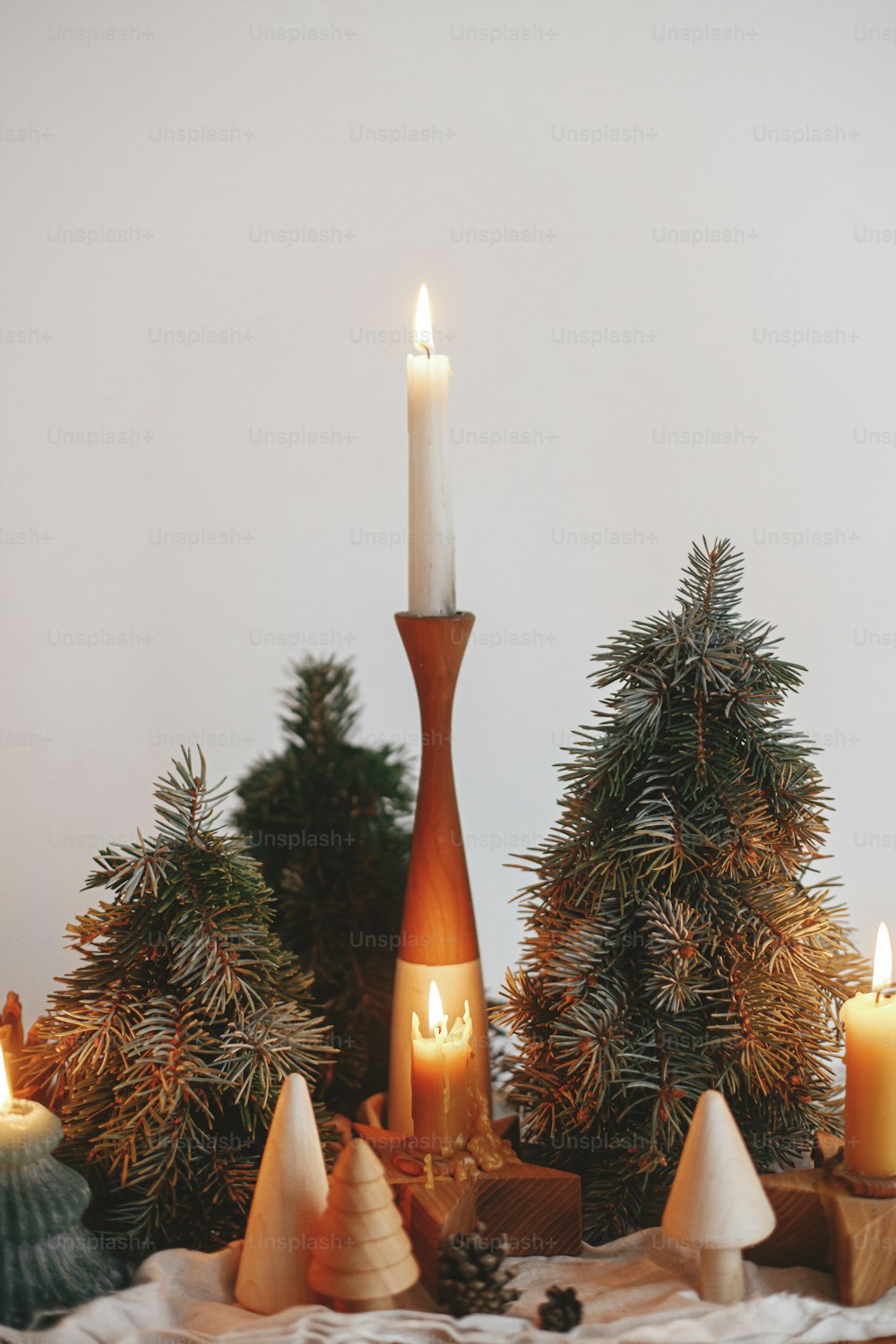 Holiday advent. Stylish christmas candles and pine trees decorations on wooden table on background of white wall in modern scandinavian festive room. Atmospheric winter time.