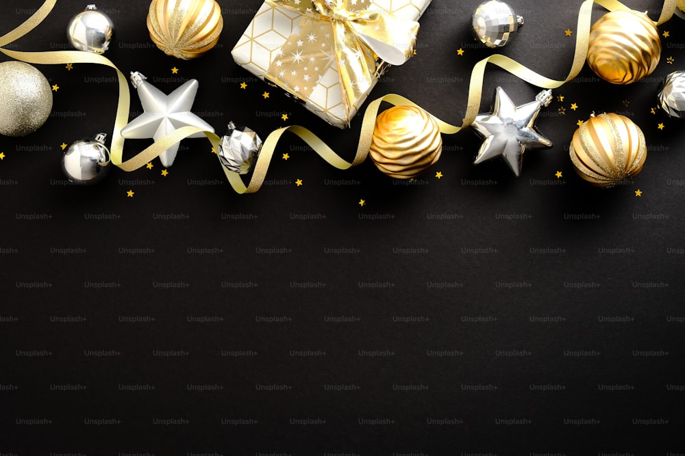 Composizione natalizia. Decorazioni di stelle e palline di Natale dorate e argentate, confezione regalo su sfondo nero scuro. Design del biglietto di auguri di Natale o Capodanno. Posa piatta, vista dall'alto, spazio di copia.