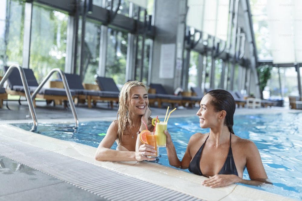 女性の友人は、プールバーでカクテルモヒートを飲み、熱帯の島のビーチ近くのビキニの高級ホテルを着てリラックスします。プールで楽しんだり、カクテルを飲んだり、笑顔を浮かべている美しい若い女性。