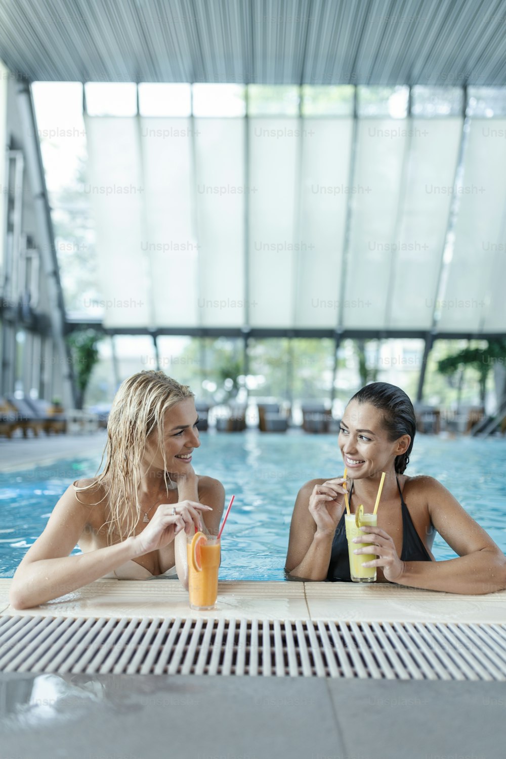 Amigos junto a la piscina relajándose tomando bebidas saludables. Mujeres jóvenes sensuales que se relajan en la piscina del balneario, piscina cubierta del balneario