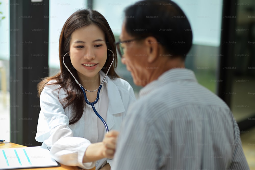 Young asian female doctor examining middle aged male patient in hospital office. Healthcare medical people concept.