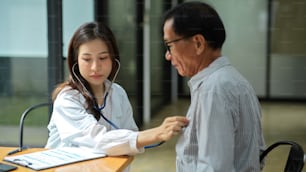 A young female doctor uses a stethoscope to check the pulse of an aged male patient. heart rate, heart beat.