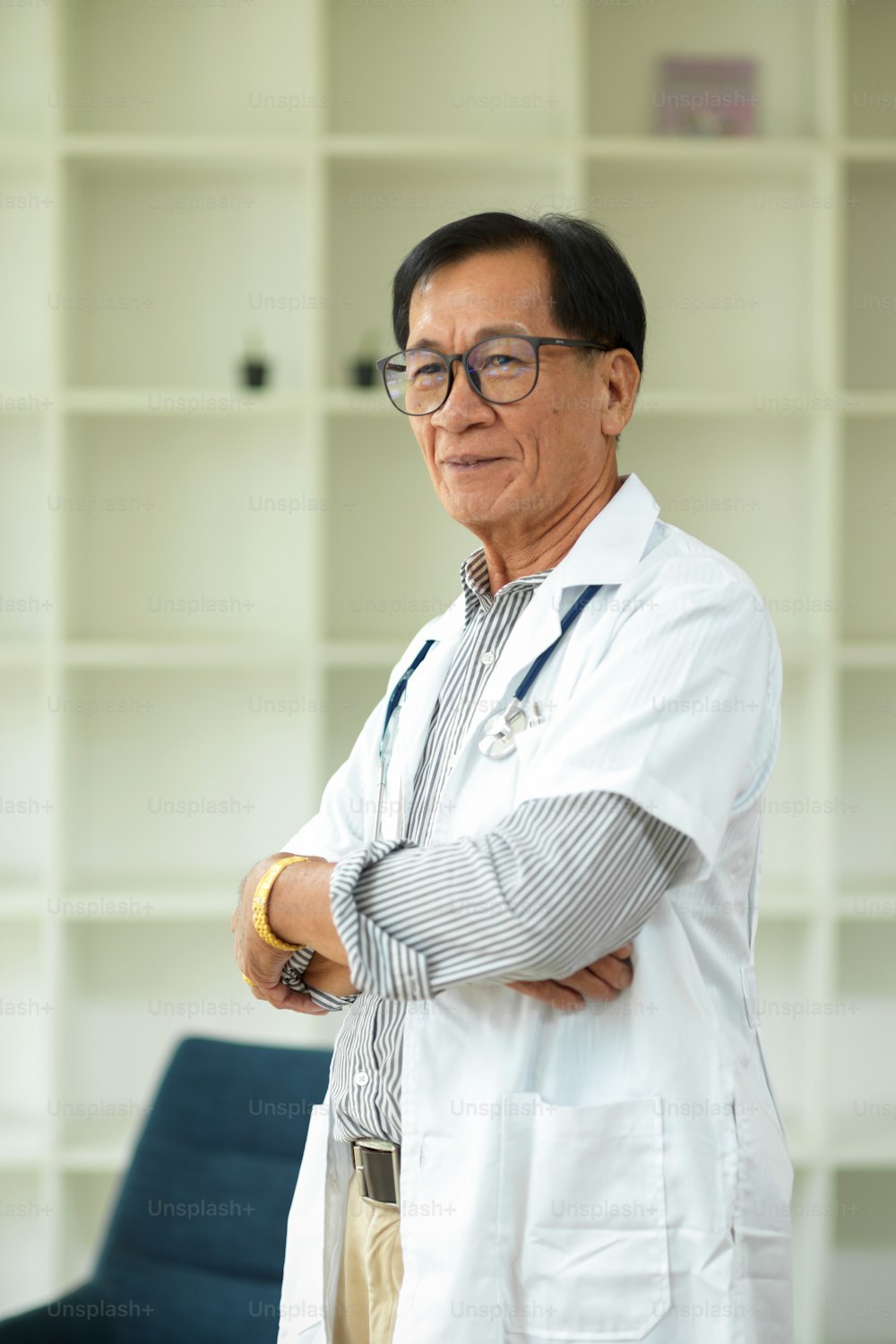 Portrait of a middle-aged male specialist and successful doctor in a white medical gown with his arms crossed in the office.