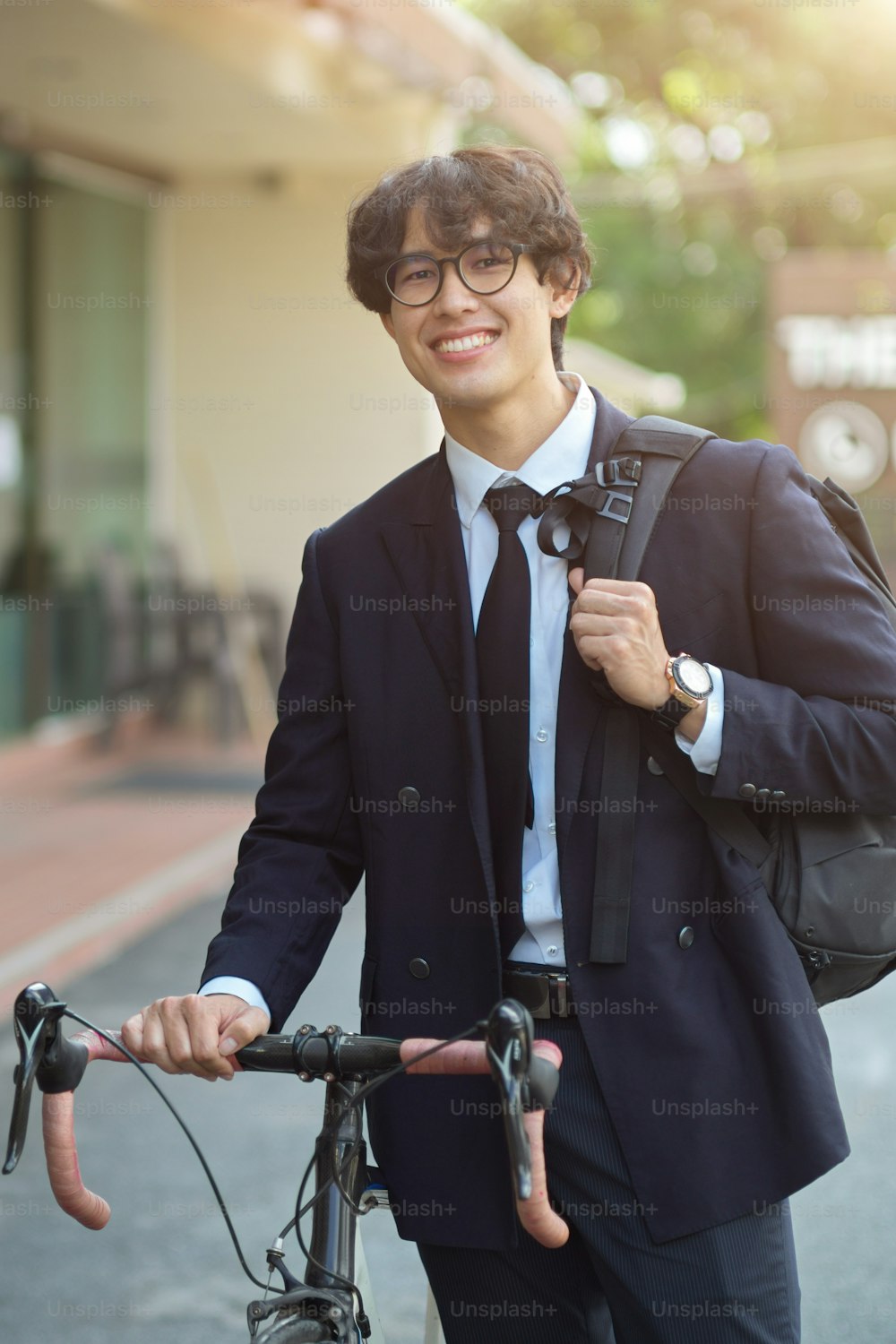 Portrait of cheerful millennial businessman in business suit walking with his bicycle on the street.