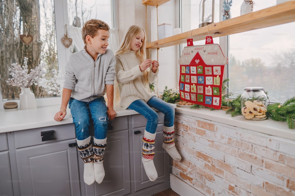 Niños leyendo tareas del calendario de adviento navideño hecho a mano en forma de casa para contar los días hasta Navidad en la pared de la habitación.