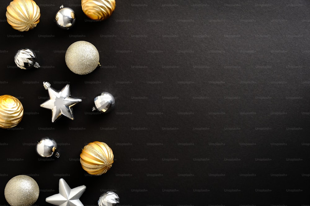 Decoración de bolas de Navidad y estrellas doradas y plateadas sobre fondo negro con espacio de copia. Tarjeta de felicitación de Feliz Navidad y Próspero Año Nuevo. Estilo minimalista. Plano, vista superior.