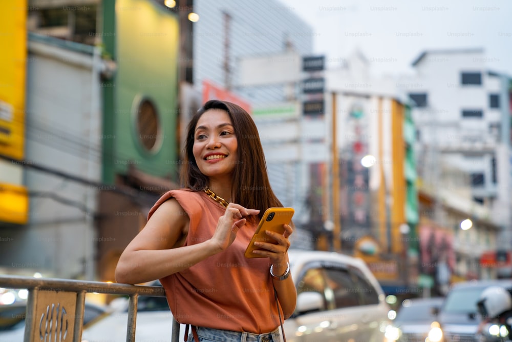 저녁에 태국 방콕 시내의 차이나타운에서 여행하고 쇼핑하는 아시아 여성. 스마트폰을 사용하여 길거리 음식과 레스토랑을 검색하는 여성 관광객은 도시 거리 야시장을 걷고 있습니다.