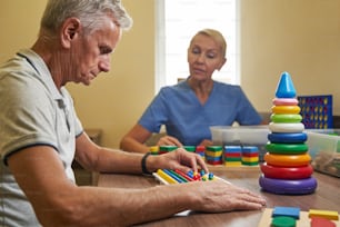 病院内セラピールームでの様々な色のペグボードを用いた脳卒中男性患者の手機能トレーニングの写真