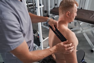 男性の患者の肩にテープを貼るプロの理学療法士。背中の痛みのキネシオテーピング