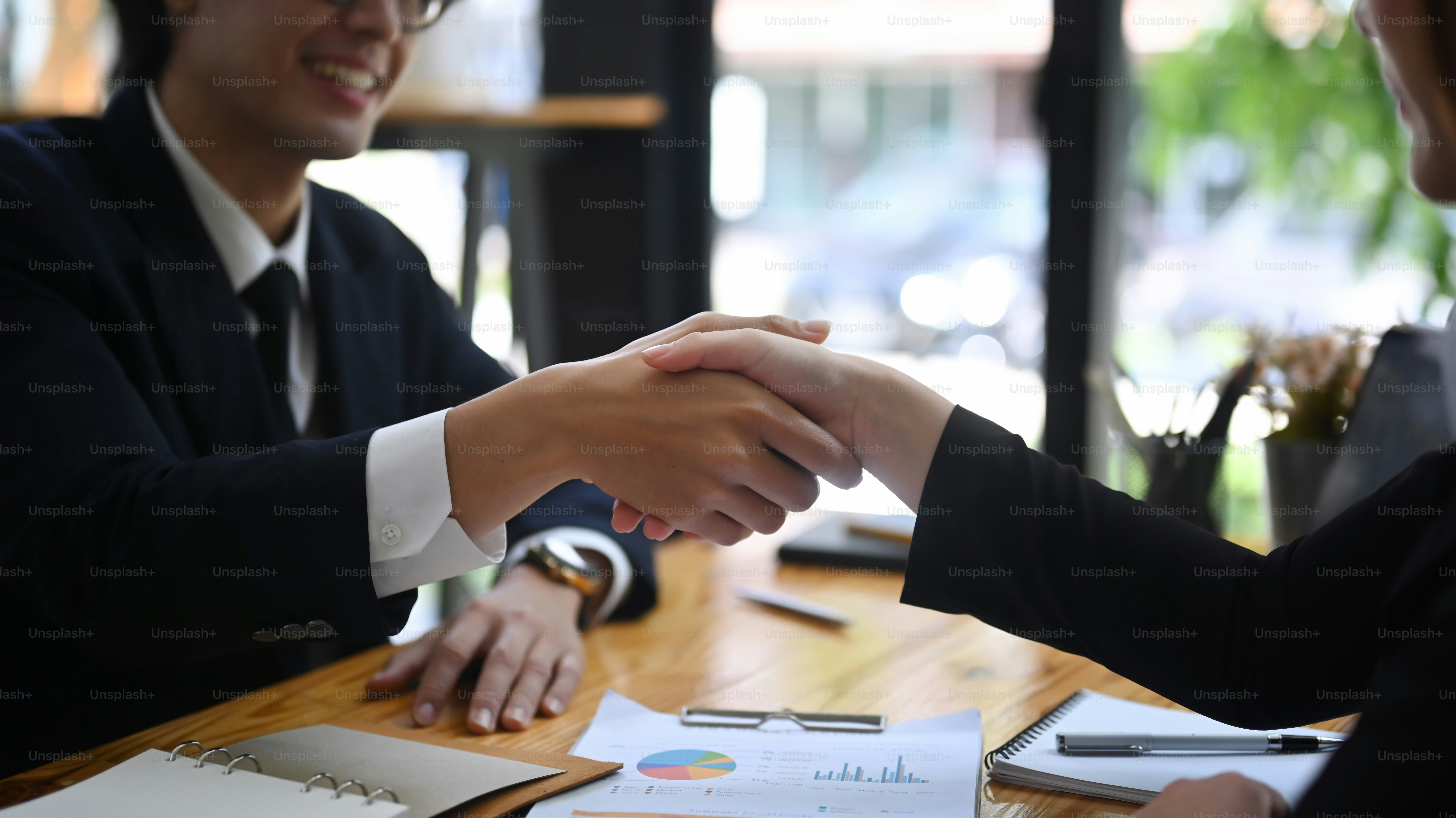 Businessmen in formal wear shaking hands after negotiations, finishing up meeting.