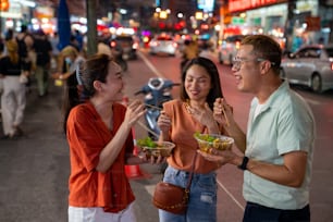 아시아 여성과 LGBTQ 친구들의 4K 그룹은 태국 방콕의 차이나 타운 거리 야시장에서 매운 소스를 곁들인 전통 길거리 음식 바베큐 해산물 구이 오징어를 함께 먹는 것을 즐깁니다.