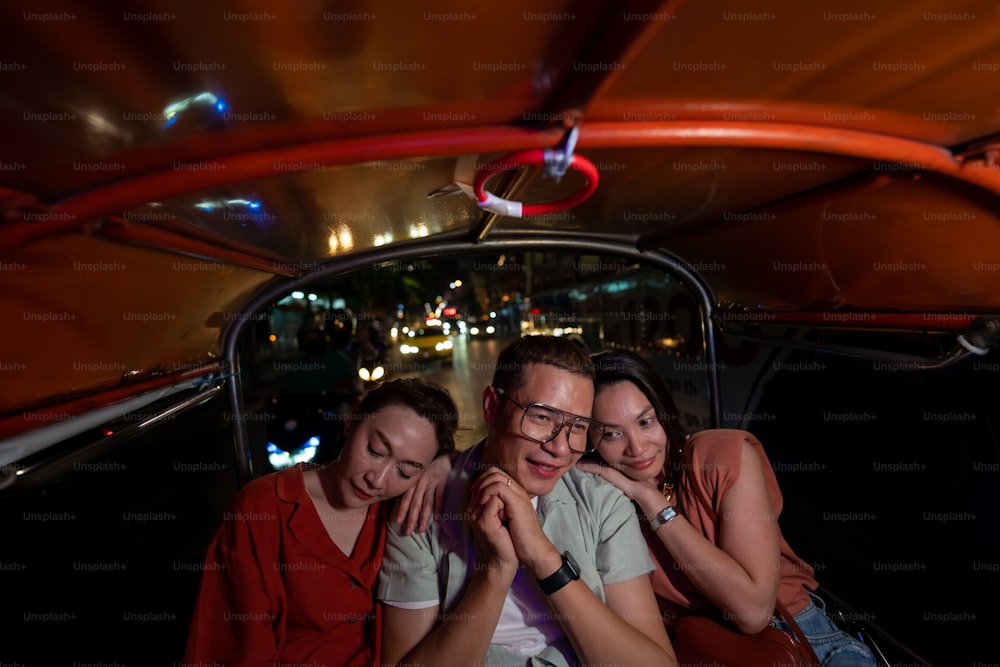 夜にトゥクトゥクタクシーでバンコク市内を旅するアジア人観光客のグループ。男性と女性の友人は、タイのアウトドアライフスタイル旅行、街の通りのナイトライフを楽しんでいます。