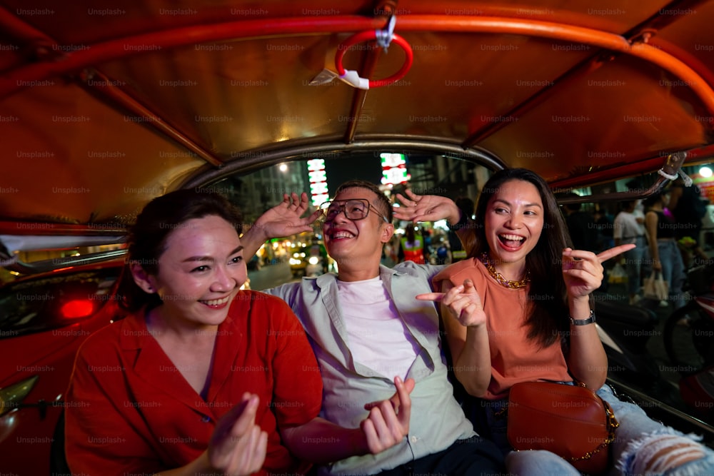 밤에 툭툭 택시차로 방콕 시내를 여행하는 아시아 관광객 그룹. 남녀 친구들은 태국에서 야외 라이프 스타일 여행 도시 거리의 밤문화를 즐기고 즐깁니다.