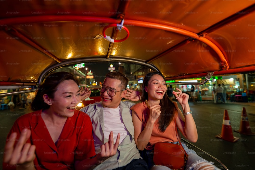 Group of Asian people tourist traveling in Bangkok city by Tuk Tuk taxi car together at night. Male and female friends enjoy and having fun outdoor lifestyle travel city street nightlife in Thailand.