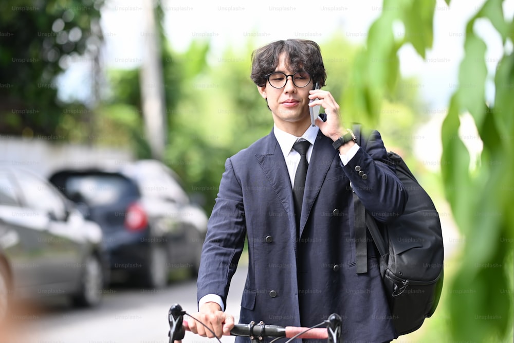 Homme d’affaires marchant dans la rue de la ville avec un vélo et parlant au téléphone portable.