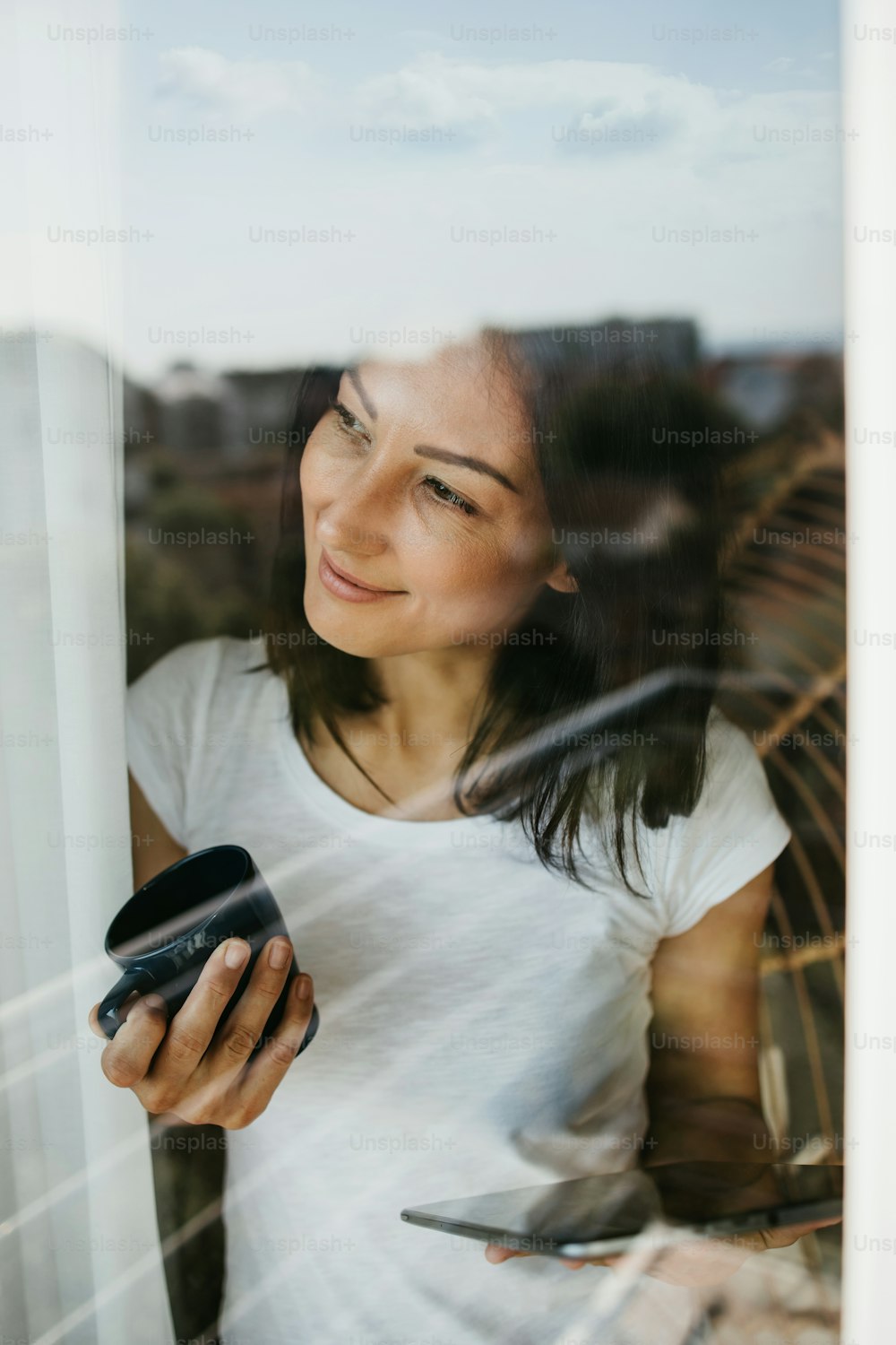 Una mujer sonriente y positiva mira por la ventana de su apartamento u oficina. Concepto de cuarentena y distanciamiento social. Mantente positivo.