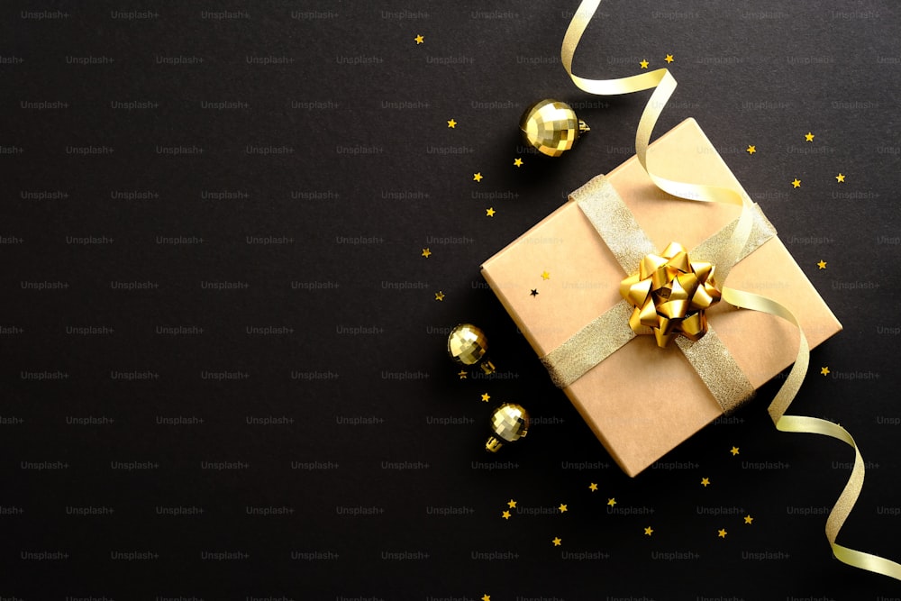 황금 공, 파티 스트리머 리본, 어두운 검은색 배경에 색종이가 있는 세련된 크리스마스 선물. 크리스마스, 블랙 프라이데이, 생일 컨셉