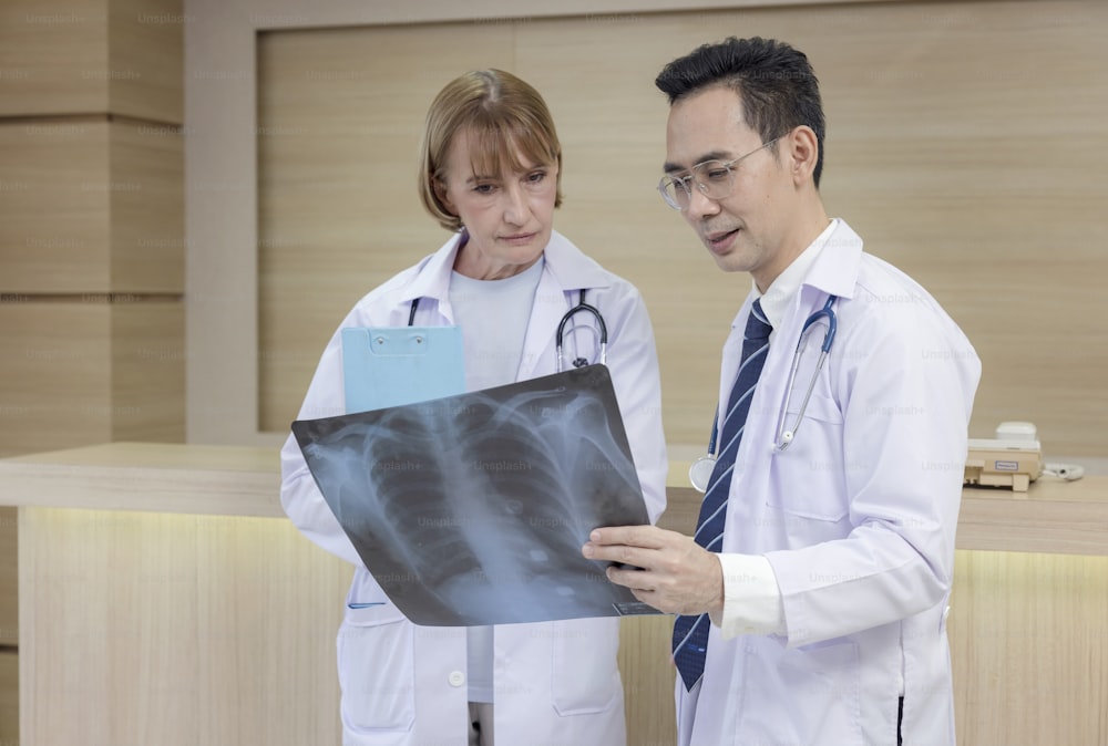 X-ray prints are examined by hospital staff. While looking at an x-ray image, two male medics confer. Two Caucasian doctors examine an MRI image and discuss it.