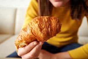 Fresh croissant in the hand of a girl having breakfast, close up