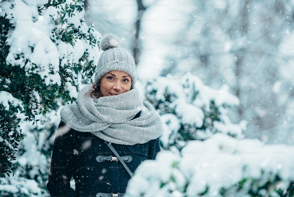 雪の中の寒い冬の日にスカーフと帽子を身に着けた美しい若い女性