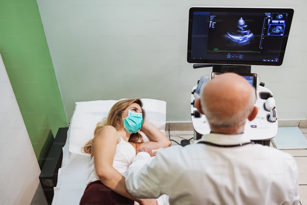 숙련 된 수석 의사가 젊은 여성 환자에게 심장 검사를 수행합니다. 그는 심장학 스캐너를 사용하고 있습니다. 의학과 현대 기술 개념.