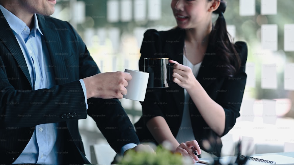 Erfolgreiche Geschäftsleute stoßen Tassen Kaffee an, um nach erfolgreicher Erledigung wichtiger Arbeit gemeinsam zu feiern.