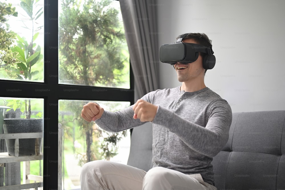 Hombre sonriente jugando videojuegos con auriculares de realidad virtual en casa.