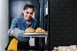 young Latin woman baking croissant on oven in kitchen in Mexico Latin America