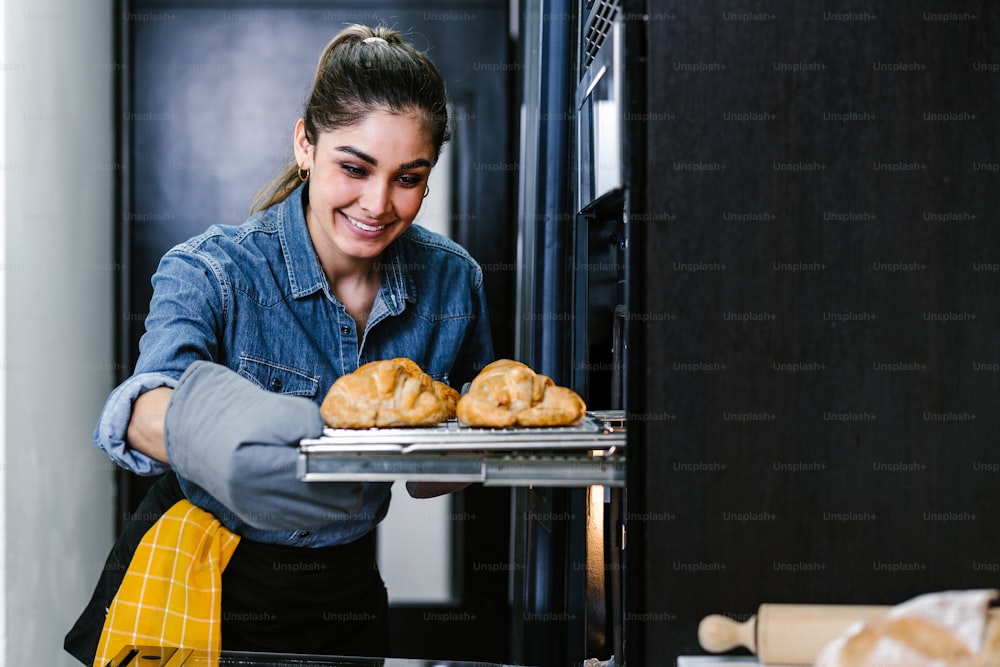 멕시코 라틴 아메리카의 부엌에서 오븐에서 크로와상을 굽는 젊은 라틴 여성