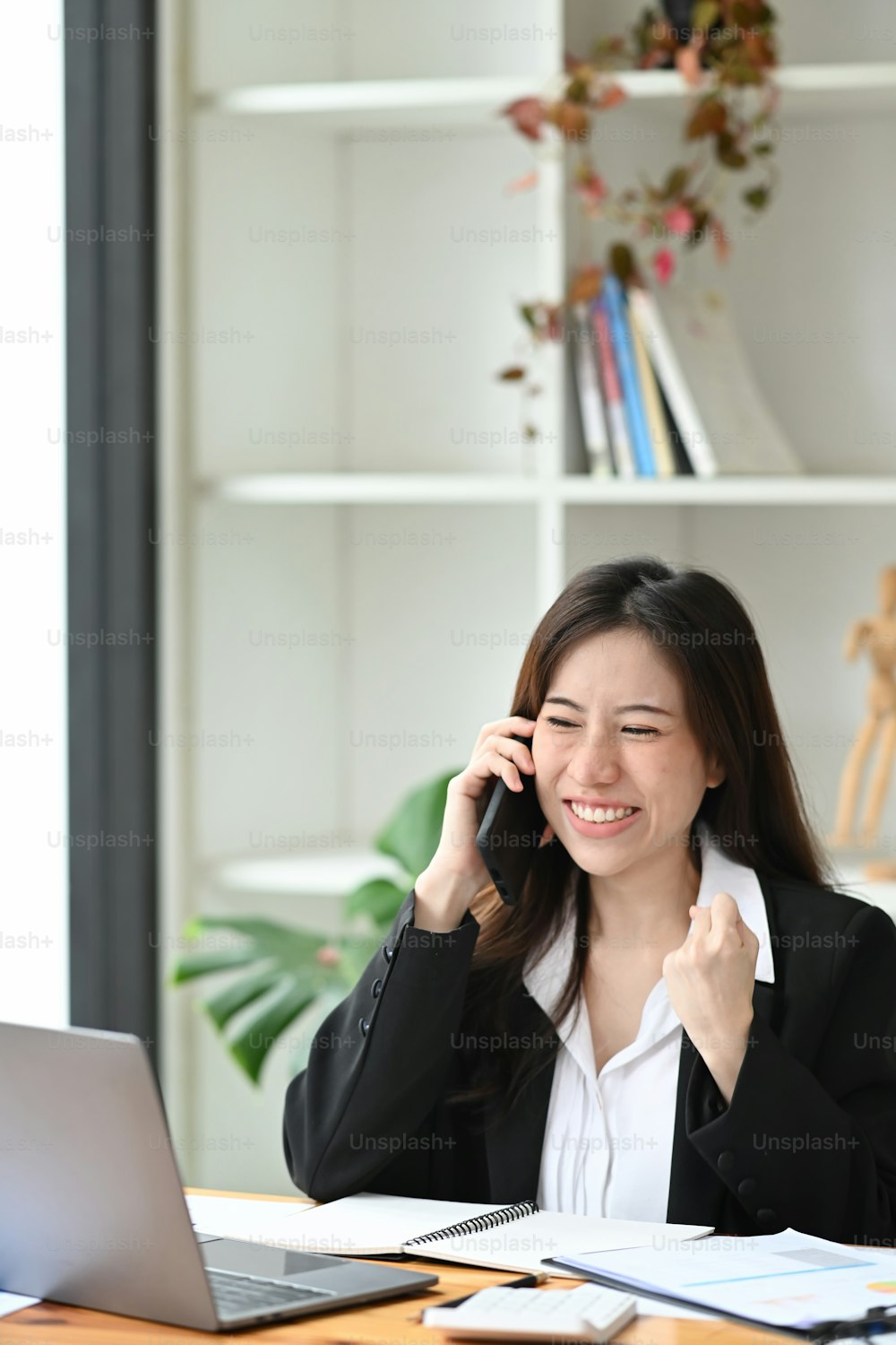 Mujer de negocios sonriente hablando por teléfono móvil y verificando información en una computadora portátil.