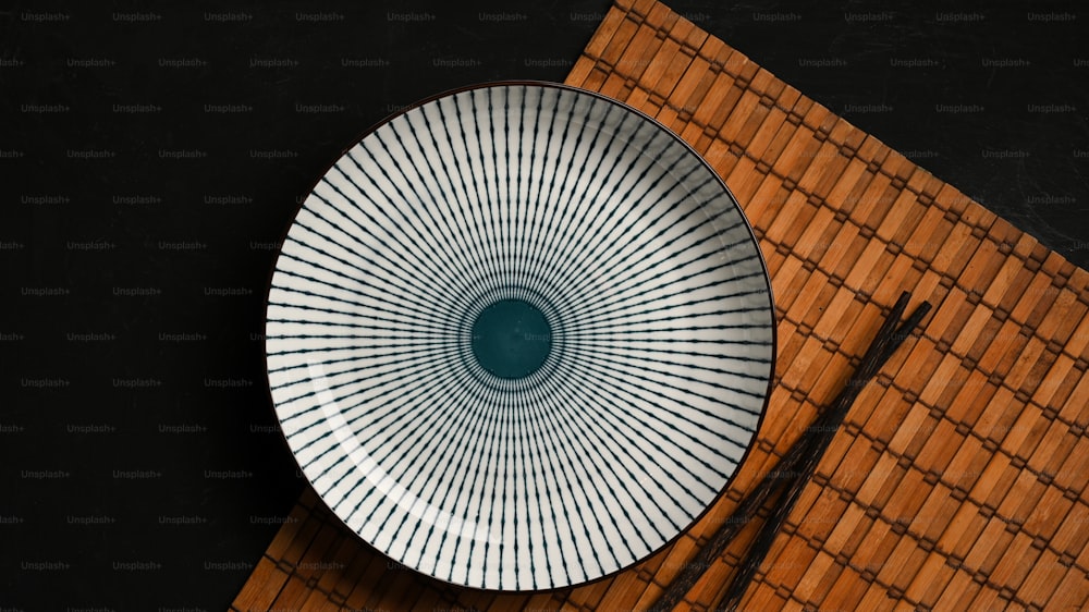 Ajuste de mesa com placa de cerâmica azul e branca com pauzinho sobre tapete de bambu em mesa escura. vista superior, flat lay