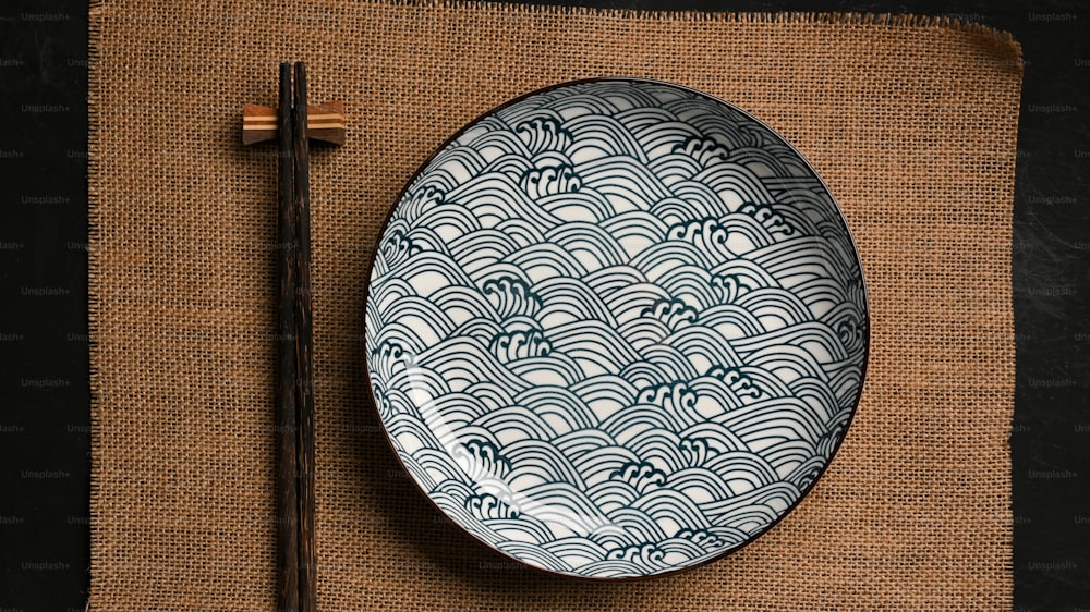 Asiatisches Geschirrkonzept, Keramikteller mit Essstäbchen auf braunem Tischset. Porzellan, blau-weiße Schale. Draufsicht