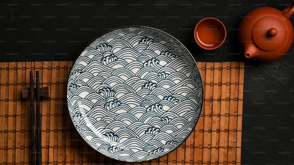 Tischdekoration im asiatischen Stil mit Porzellanteller mit Essstäbchen und asiatischem Teeservice auf dem Esstisch. Draufsicht