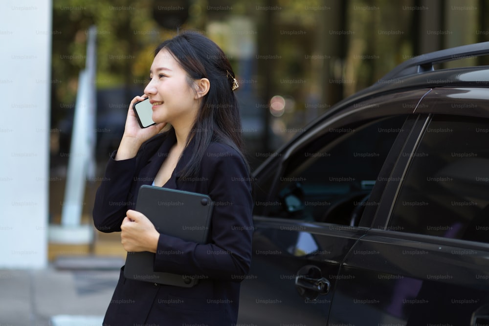 Une femme entrepreneure confiante et prospère qui parle au téléphone, debout près de sa voiture. Concept de vie urbaine et d’hommes d’affaires.