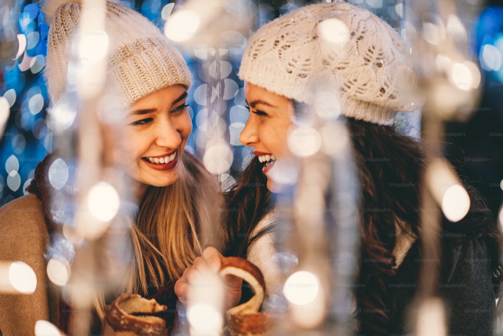 Glückliche junge Freundinnen, die Spaß haben und Momente zusammen im weihnachtlich geschmückten Hintergrund genießen.
