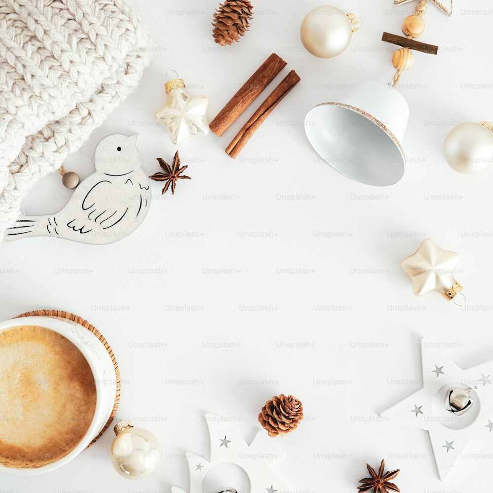 크리스마스 구성입니다. 북유럽 스타일의 나무 크리스마스 장식, 커피 한 잔, 계피 스틱, 종, 흰색 테이블 상단 뷰에 베이지 색 공. 휘게, 보헤미안 홈 데코.