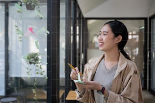 Smiling creative woman reading sticky notes on glass wall in modern workplace.