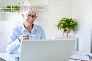 Mujer con gafas en casa concentrándose mientras trabaja en una computadora portátil. Mujer de mediana edad que trabaja desde casa en una computadora portátil. Retrato de una mujer madura ejecutiva escribiendo en una computadora portátil mientras trabaja en casa.