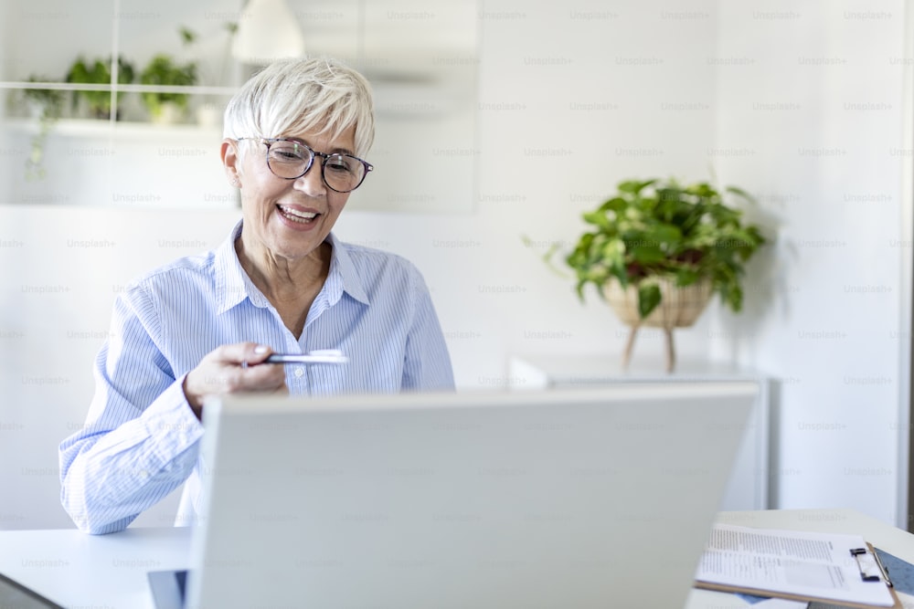 Frau mit Brille zu Hause, konzentriert an einem Laptop arbeitend. Frau mittleren Alters, die von zu Hause aus am Laptop arbeitet. Porträt einer reifen Führungsfrau, die auf dem Laptop tippt, während sie zu Hause arbeitet.