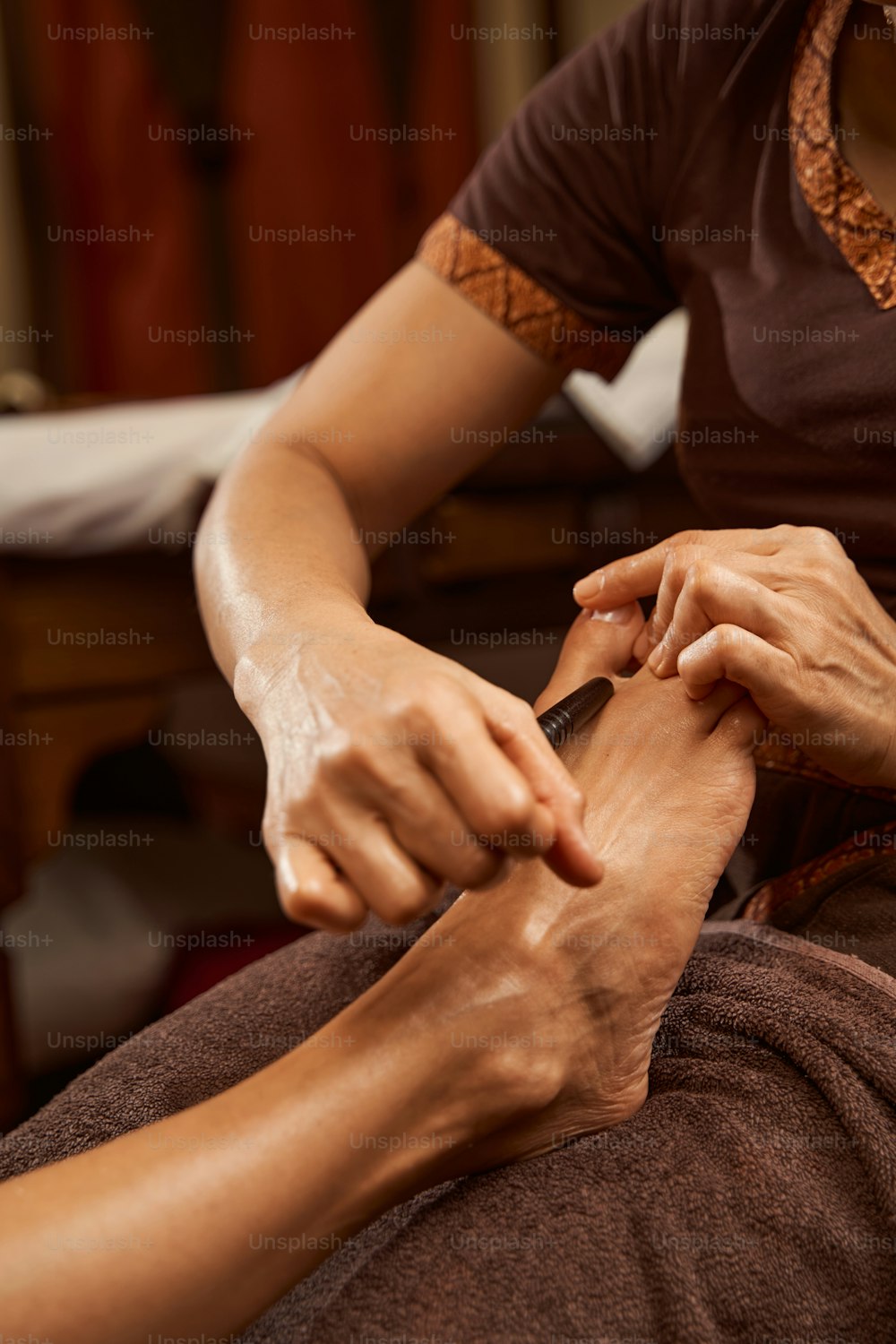 Foto ritagliata del riflessologo che fa un massaggio tailandese ai piedi usando il bastone per riflessologia