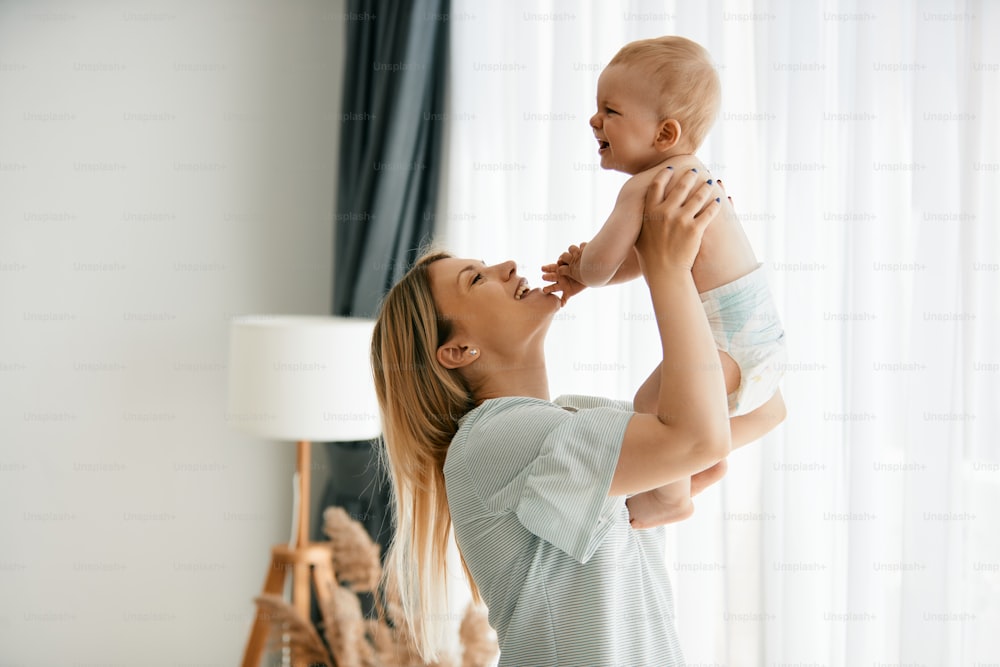 Happy mother trying to cheer up her crying baby boy while playing with his at home.