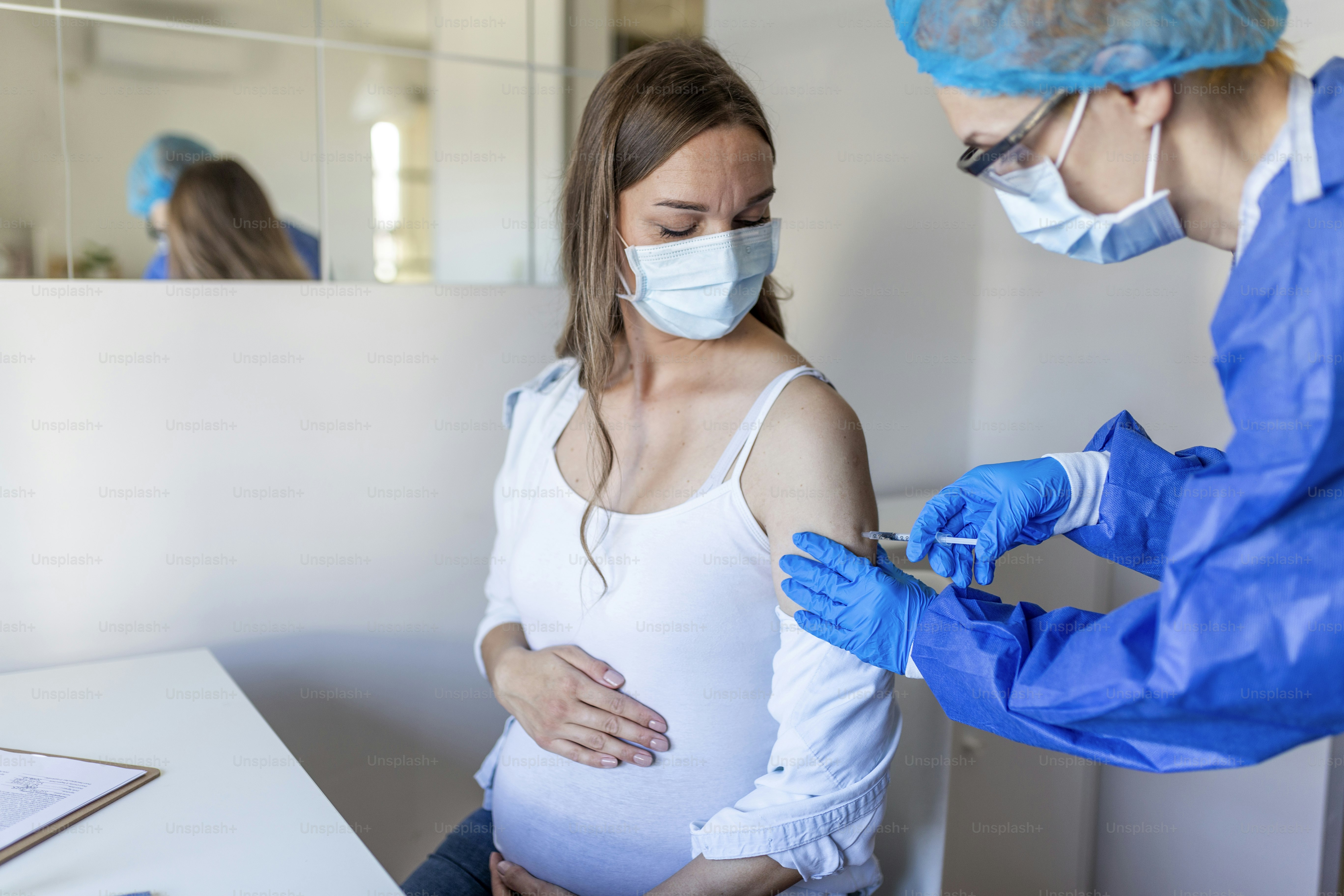 Pregnant Vaccination. Doctor giving COVID -19 coronavirus vaccine injection to pregnant woman. Doctor Wearing Blue Gloves Vaccinating Young Pregnant Woman In Clinic. People vaccination concept.