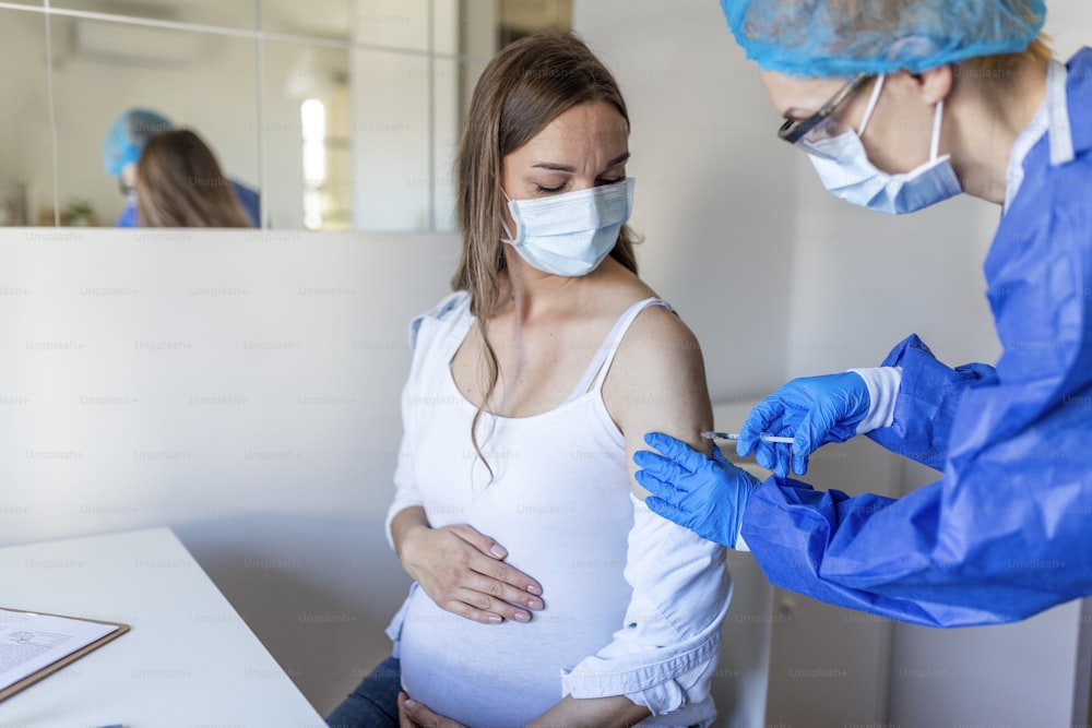 Vacinação de Gestantes. Médico que administra injeção de vacina contra o coronavírus COVID-19 a gestante. Médico usando luvas azuis vacinando jovem grávida na clínica. Conceito de vacinação de pessoas.