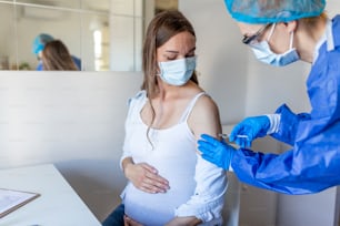 Schwangere Impfung. Arzt, der einer schwangeren Frau einen COVID-19-Coronavirus-Impfstoff verabreicht. Arzt mit blauen Handschuhen impft junge schwangere Frau in der Klinik. Impfkonzept für Menschen.