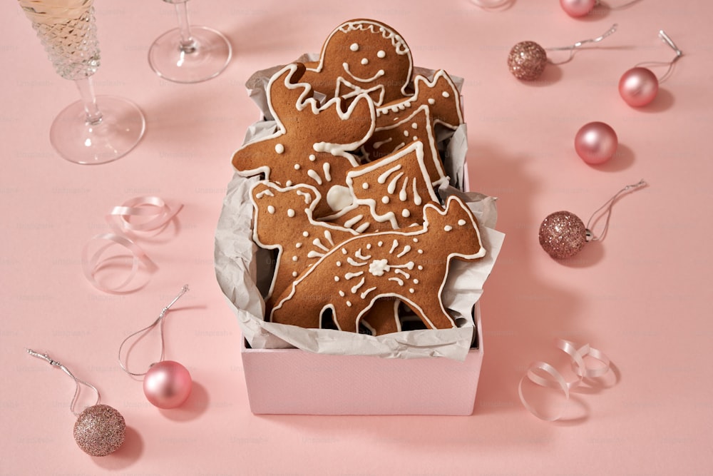 Homemade gingerbread cookies in a gift box with Christmas ornaments and champagne on pink background